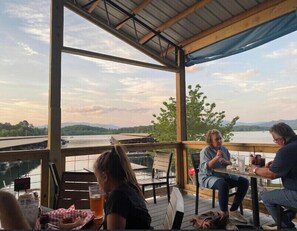 A covered outdoor seating area with a view of a lake and mountains. - Riverfront Cabin! Mountain Views, Pool, Hot Tub, Fishing, Tubing, Fire Pit, WIFI (Hiawassee)