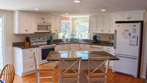 Una cocina con armarios blancos, microondas integrado, estufa, refrigerador y una barra desayunadora con sillas.