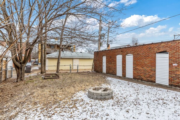 A brick building with a fire pit in the yard, surrounded by leafless trees and a snow-covered ground. - Dog-Friendly South City 1st Floor Apartment (St. Louis)