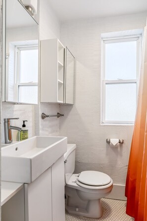 Un baño con lavamanos blanco, inodoro, espejo y ventana.