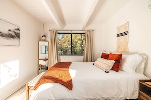 A bedroom with a large bed, a window with curtains, a mirror, and a wall-mounted tapestry.