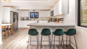 A modern kitchen with white cabinetry, a central island, and bar stools. - Family & Pet-Friendly, Cozy & Stylish Cabin Steps from Lake+Village (Lake Arrowhead)