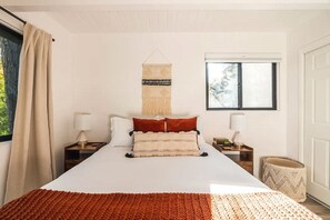 A bedroom with a large bed, two bedside tables, a hanging tapestry, and a window with a view.