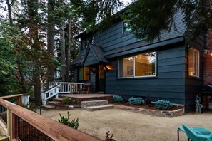 Une cabane en bois sombre, dotée d’une terrasse et entourée d’arbres.