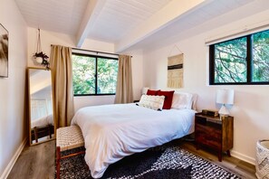A bedroom with a large bed, a bedside table, a mirror, and a window with curtains. - Black Pine - 4BR Lake Arrowhead Cabin | Family & Pet-Friendly (Lake Arrowhead)
