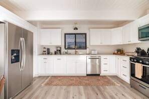 Una cocina moderna con armarios blancos, electrodomésticos de acero inoxidable y un amplio ventanal.