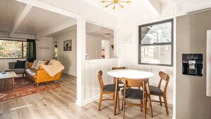 A spacious room with a wooden dining table, chairs, a sofa, and a ceiling light fixture. - Family & Pet-Friendly, Cozy & Stylish Cabin Steps from Lake+Village (Lake Arrowhead)