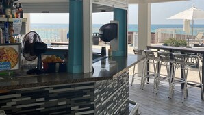A covered outdoor bar area with a view of the ocean, bar stools, and a fan. - Beachfront condo in Miami! (Sunny Isles Beach)