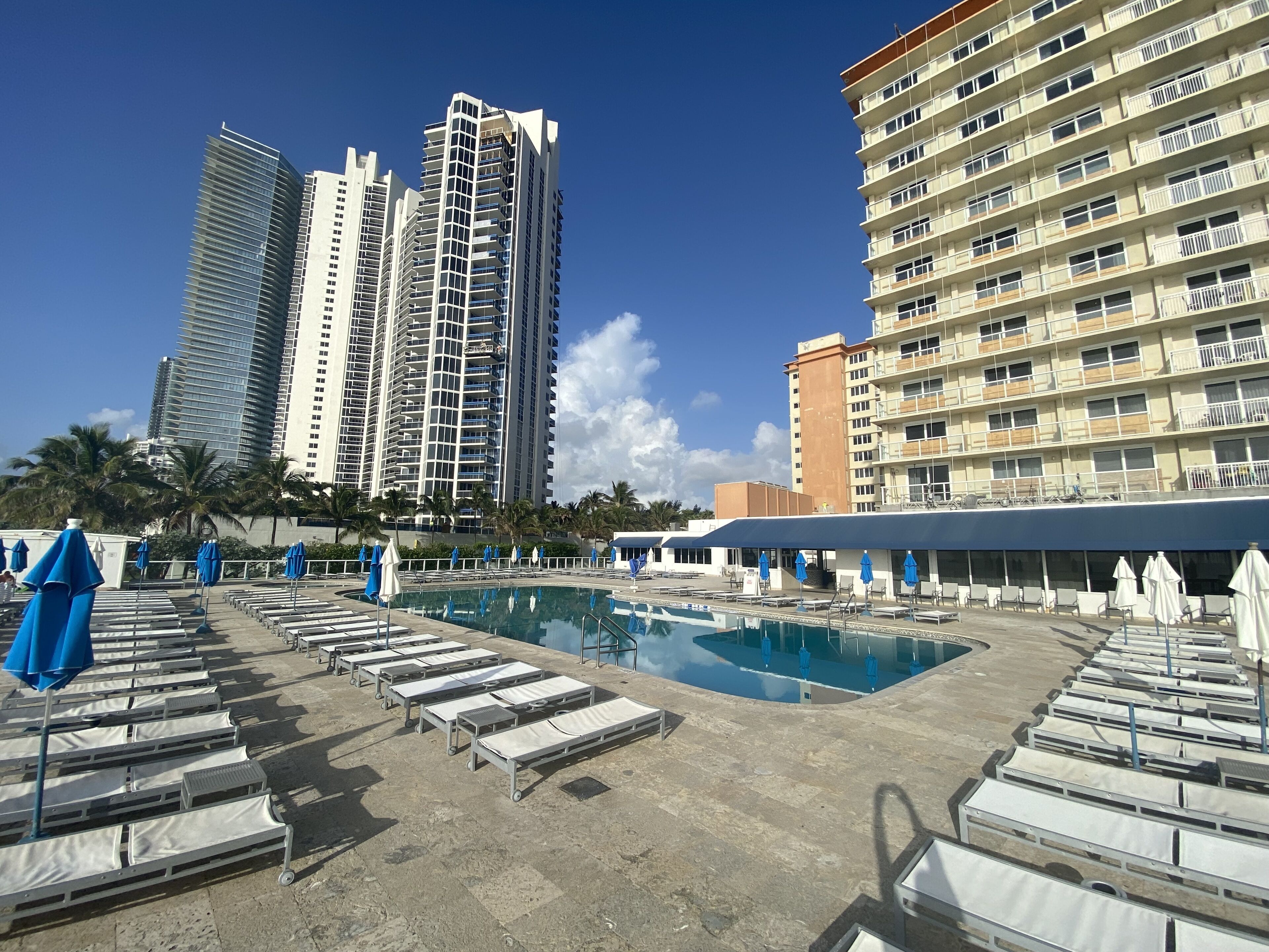 Ein Hotelpoolbereich mit Liegestühlen und Sonnenschirmen, umgeben von hohen Gebäuden.