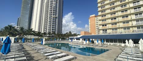 A hotel pool area with sun loungers and umbrellas, surrounded by tall buildings.
