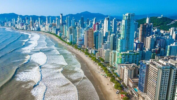 A coastal cityscape with high-rise buildings, a beach, and mountains in the background.