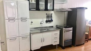 A compact kitchen with white appliances, including a refrigerator, oven, and sink. There are cabinets above the counter and a stove with a range hood.