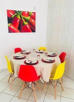 A dining area with a round table set for six, surrounded by red and yellow chairs.