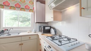 A kitchen with a gas stove, microwave, toaster, and a window with a view of trees. - A West London Retreat (London)