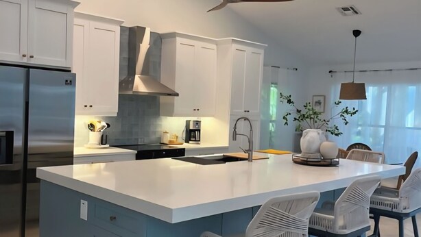 Een moderne keuken met witte kasten, een groot eiland met barkrukken, een plafondventilator en inbouwspots.