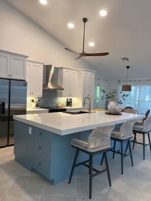 A modern kitchen with white cabinets, a large island with bar stools, a ceiling fan, and recessed lighting. - PICCADILLY MANOR-3BD/2BA W HEATED POOL  +1 773 443-7832  (Naples)