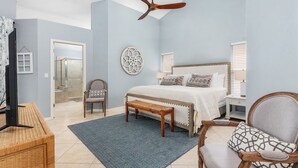 Een slaapkamer met een bed, een plafondventilator, een houten bankje, een stoel, een wanddecoratie en een raam met zonwering.