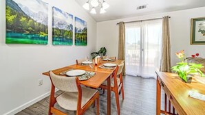 A dining area with a wooden table set for four, surrounded by chairs. There are three framed landscape paintings on the wall above the table. - Peaceful retreat near the redwoods, ocean, and golf course! (Eureka)