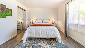 A bedroom with a bed, bedside lamps, a nightstand, a window with curtains, and a door. - Peaceful retreat near the redwoods, ocean, and golf course! (Eureka)