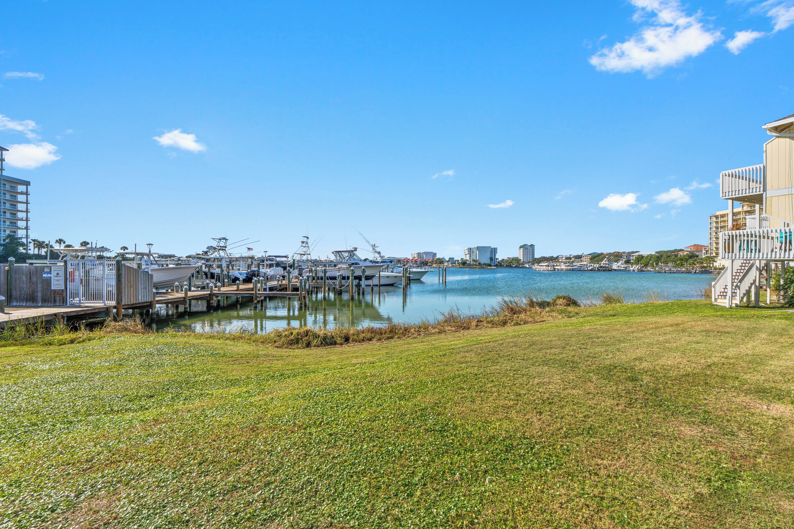 A marina with docked boats, a grassy area in the foreground, and buildings in the background.