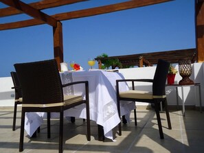 Ein Essbereich im Freien mit zwei Korbstühlen und einem Tisch, der mit einer weißen Tischdecke bedeckt ist.