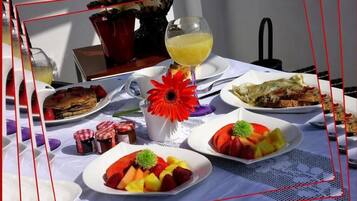 A table set with plates of fruit, a glass of orange juice, and a red flower centerpiece.