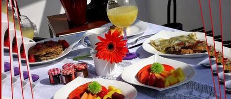 A table set with plates of fruit, a glass of orange juice, and a red flower centerpiece.