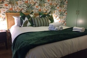 A neatly made bed with a green blanket, white pillows, and rolled towels.