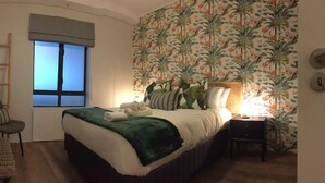 Ein Schlafzimmer mit Bett, Fenster, Sessel, Nachttisch und Wand mit Blumenmuster.