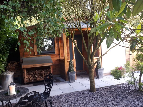 A wooden cabin with a fireplace, surrounded by trees and potted plants. - Ever Wanted to go off Grid,then This is for you (Sutton Coldfield)
