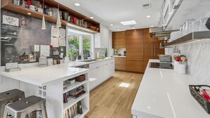 A modern kitchen with white cabinetry, wooden accents, and a central island. - 3BR Encinitas Family Retreat | Hot Tub & Fire Pit (Encinitas)