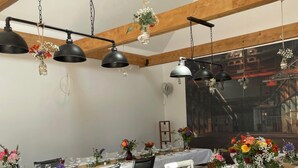 Una larga mesa de comedor dispuesta para una comida, con manteles blancos, varias sillas y lámparas colgantes.