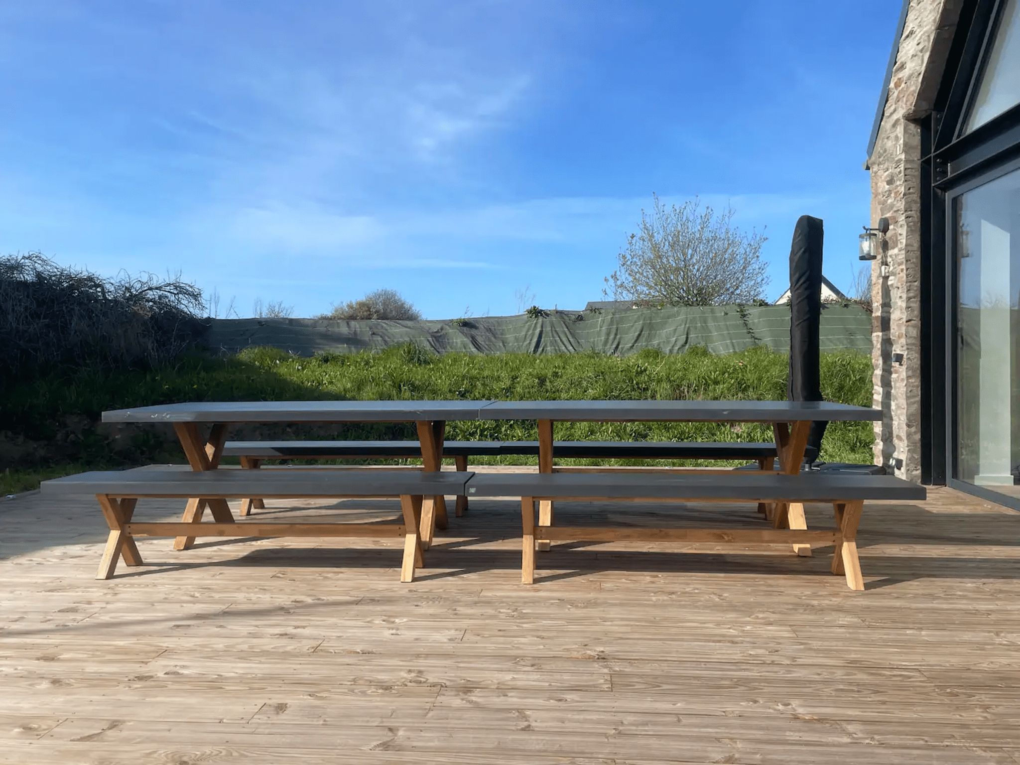 Een houten terras met picknicktafels, een stenen gebouw en een heldere lucht.