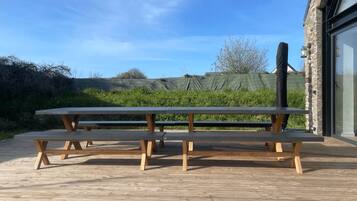 Een houten terras met picknicktafels, een stenen gebouw en een heldere lucht.