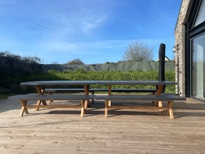 A wooden deck with picnic tables, a stone building, and a clear sky.