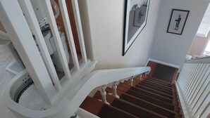 Eine Treppe mit weißen Balustern und einem hölzernen Geländer, die zu einer Empfangshalle mit weißer Wand und einem gerahmten Bild führt.