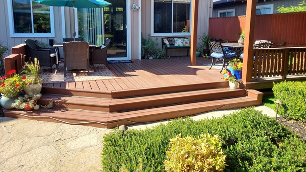 Eine Holzterrasse mit Gartenmöbeln, einer Pergola und einer Pflanzenterrasse.