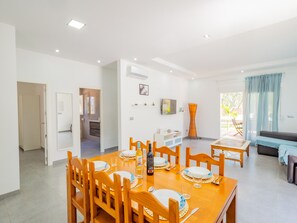 A modern dining area with a wooden table set for four, a television mounted on the wall, and a view of the outdoors through a large window.