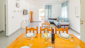 Una sala de estar moderna con un sofá, una mesa de comedor preparada para dos personas y un televisor montado en la pared.