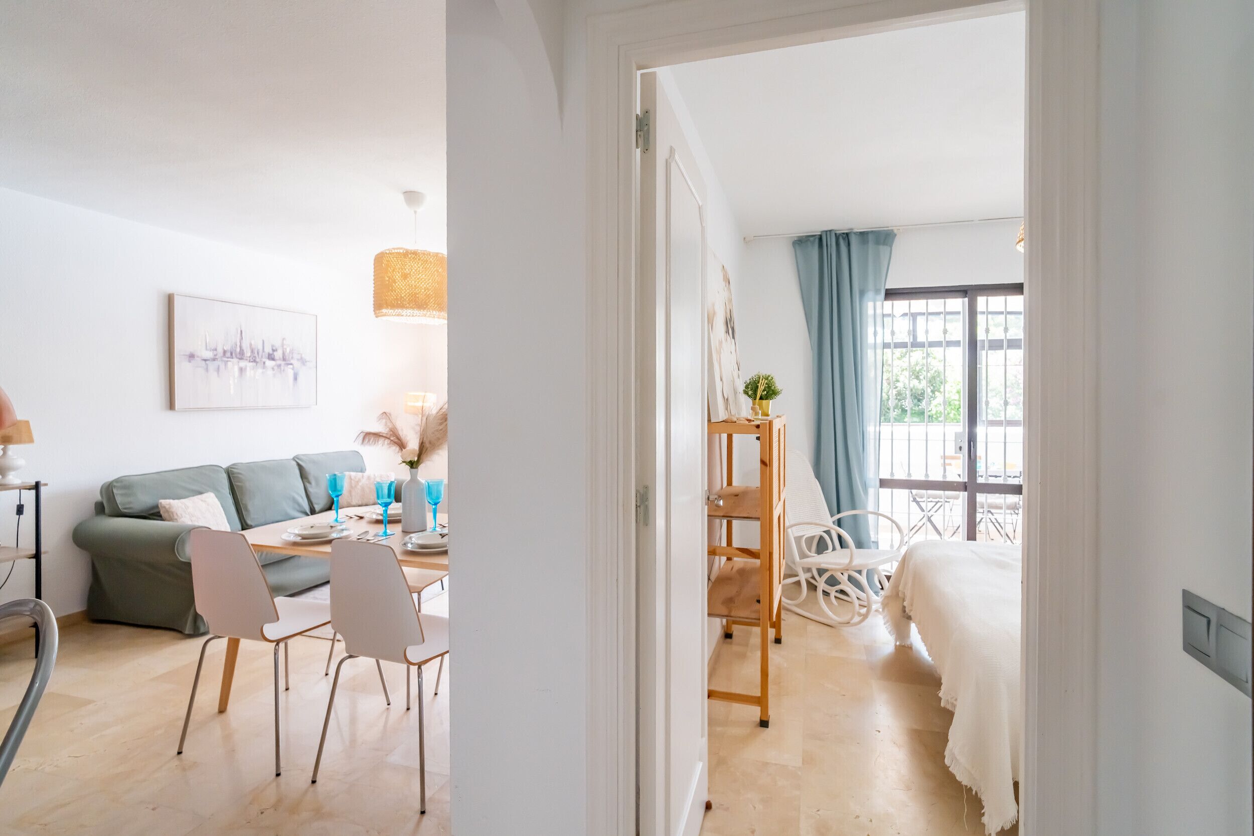 A modern hotel room with a dining area, a sofa, a bed, and a balcony with a view.