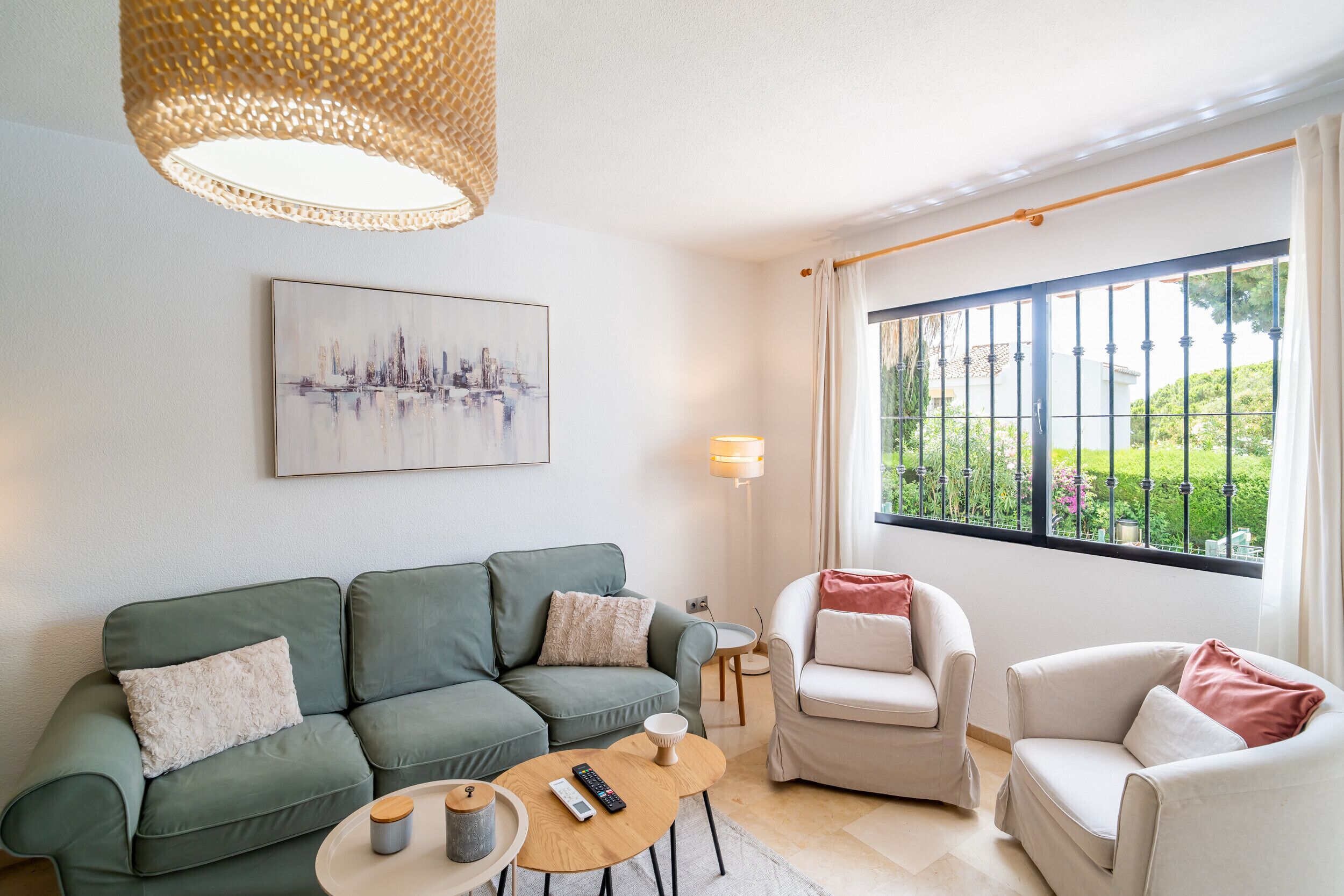 Ein modernes Wohnzimmer mit einem grünen Sofa, einem weißen Sessel, einem runden Couchtisch und einem großen Fenster mit Blick ins Grüne.