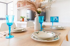 Una mesa de comedor decorada con vajilla azul, platos florales y un jarrón blanco con plantas secas.