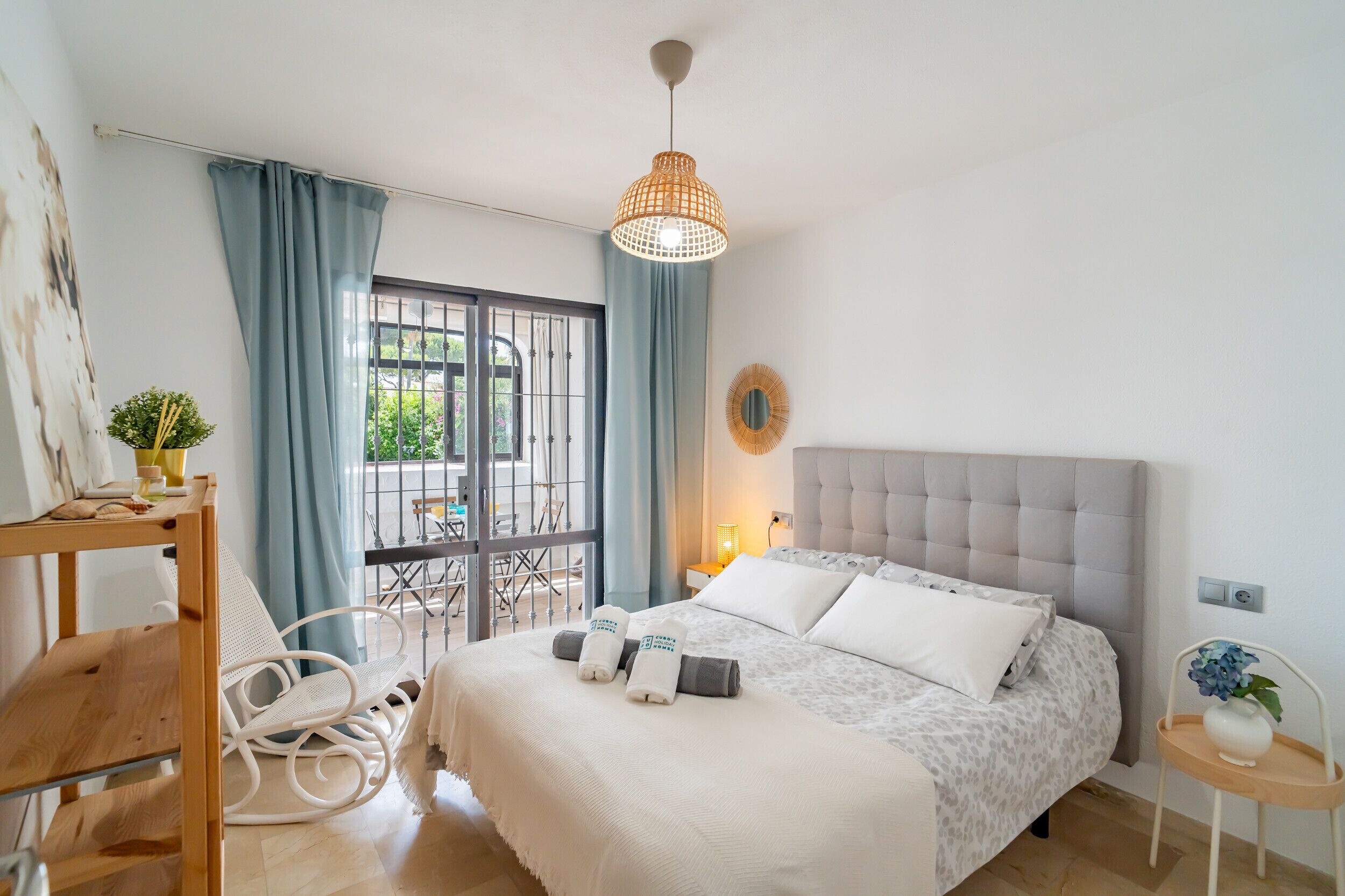 A bedroom with a bed, a chair, a table, a hanging light fixture, and a window with curtains.