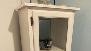 Un meuble blanc avec une porte en verre, orné d’une étoile de mer sur le dessus et contenant une petite figurine à l’intérieur.
