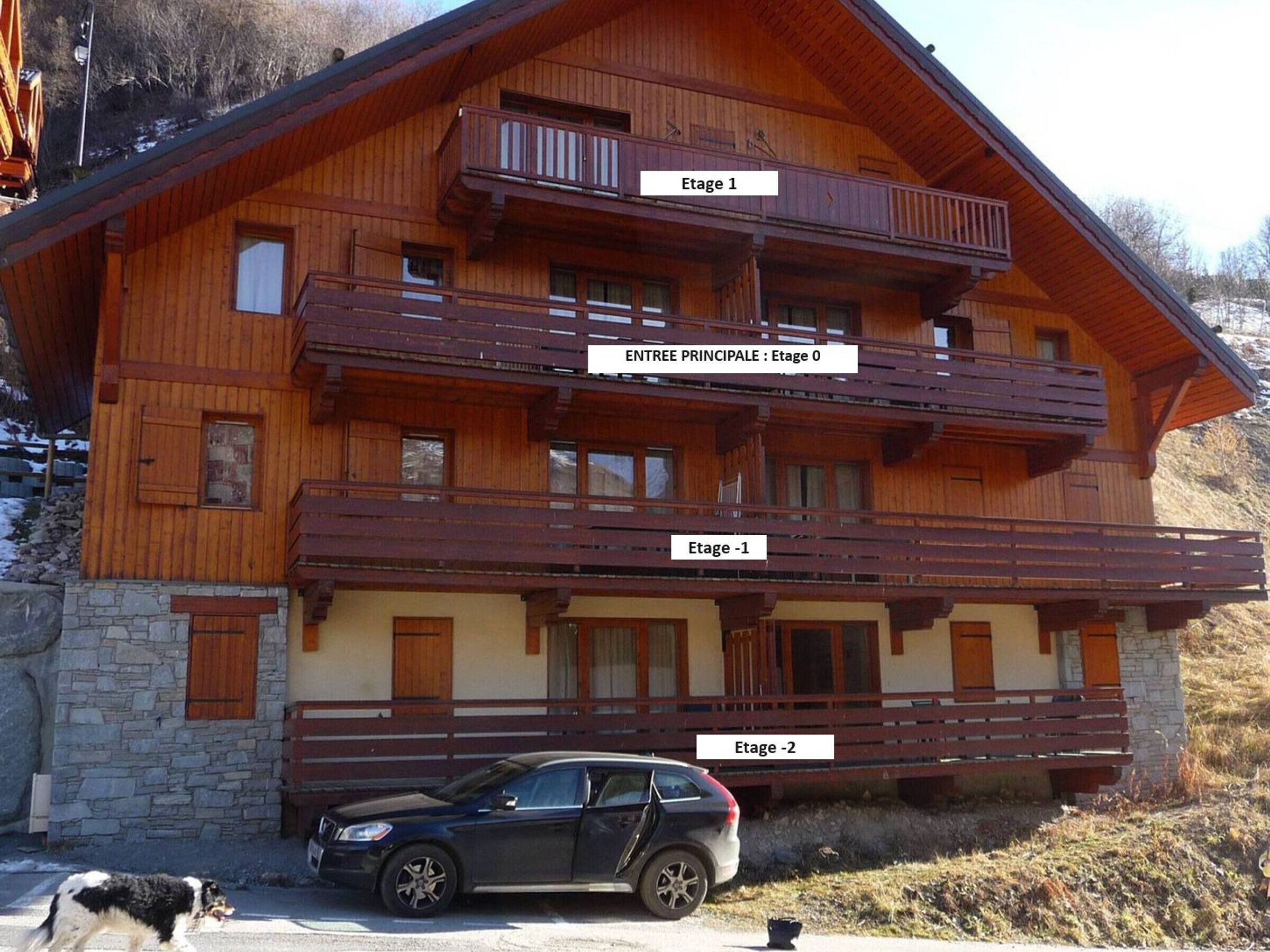 Ein mehrstöckiges Holzchalet mit Balkonen, auf denen Etage 1, Etage -1 und Etage -2 gekennzeichnet sind.