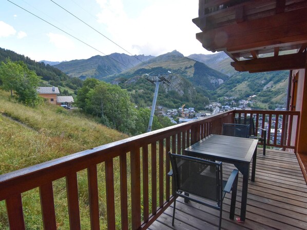 Una terraza de madera con una mesa y sillas, con vistas a un valle con casas y montañas.