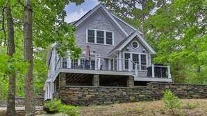 A two-story house with a stone foundation, a balcony, and a stone wall.