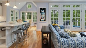 A spacious kitchen with a central island, bar stools, and a dining area with a large window overlooking greenery.