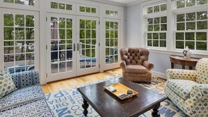 A spacious room with large glass doors leading to an outdoor deck, a leather armchair, a patterned sofa, and a wooden coffee table.
