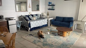 A living room with a sofa, a dining table, a coffee table, and a dog. - One Bedroom Apartment, One block from the beach BTR #2197 (Indian Rocks Beach)